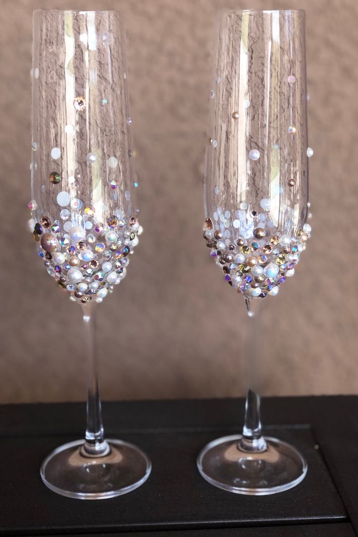 two wine glasses with beads on them sitting next to each other in front of a wall