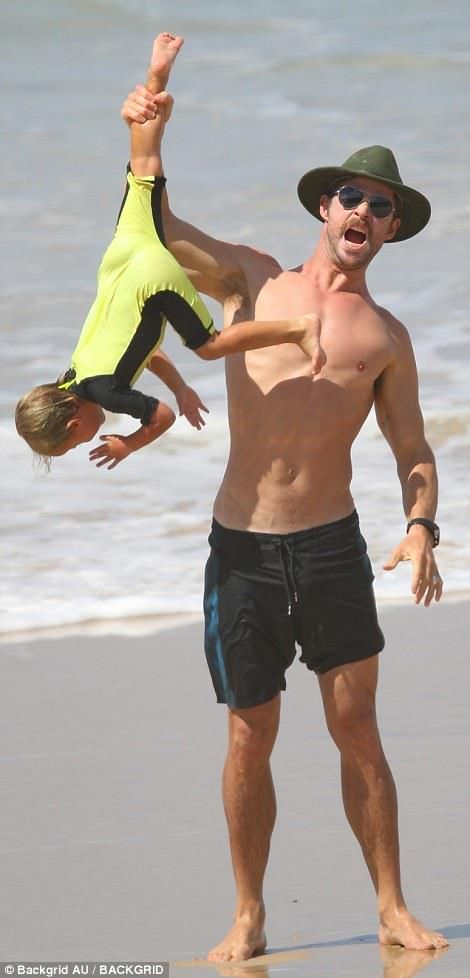 a man holding a young boy on the beach while he holds his leg up in the air