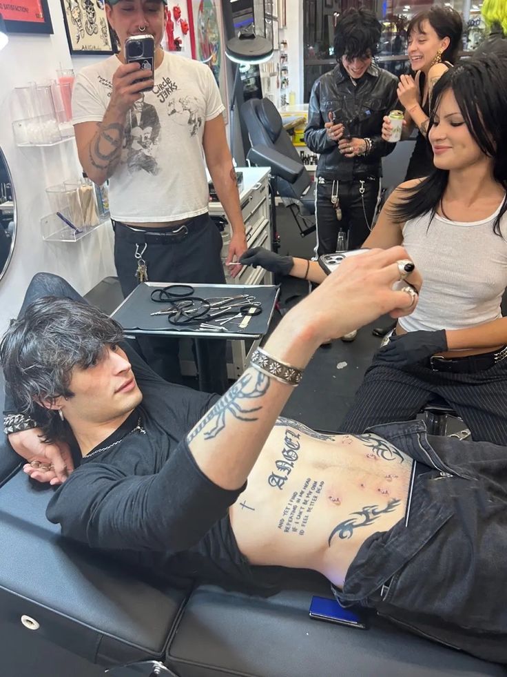 a man laying on top of a table next to a woman holding a cell phone