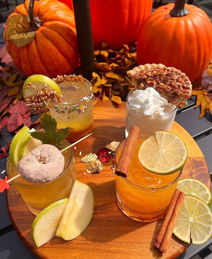 there are three drinks on the table with oranges and pumpkins in the background