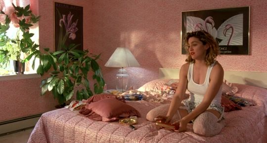 a woman sitting on top of a bed next to a plant in a pink room