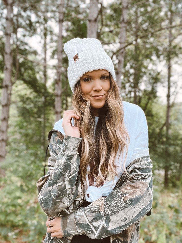 a beautiful young woman standing in the woods with her arms crossed and looking at the camera