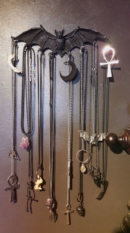 an assortment of necklaces hanging on the wall in front of a cross and devil's head