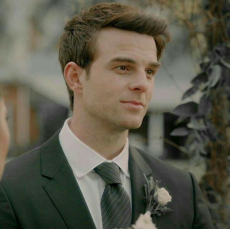 a man in a suit and tie standing next to a tree