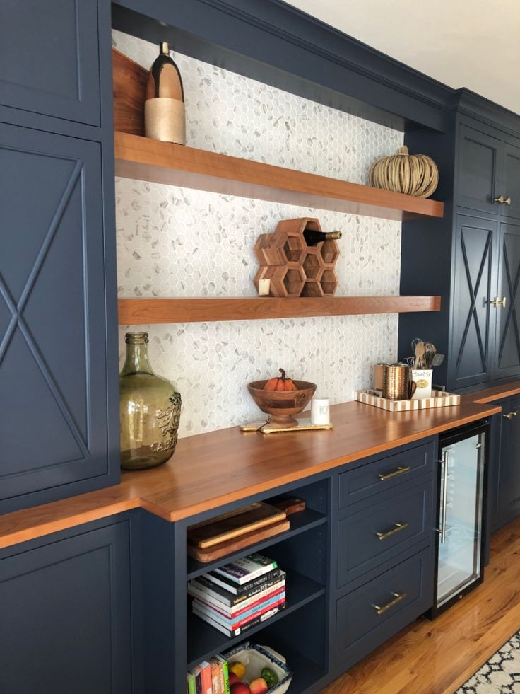 a kitchen with dark blue cabinets and wooden shelves on the wall, along with an area rug