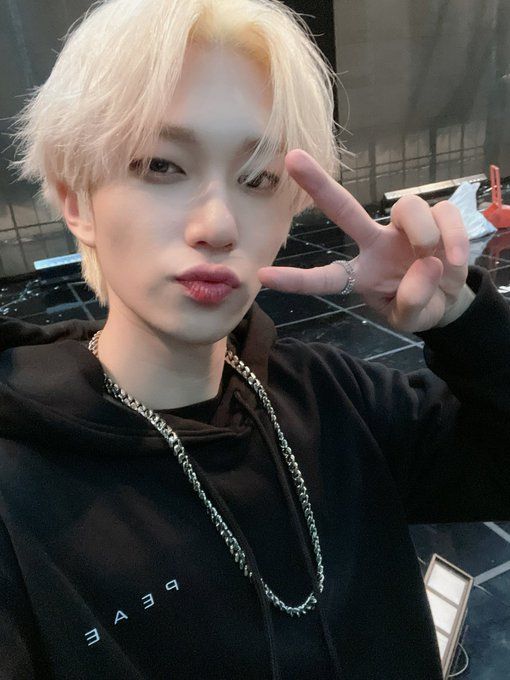 a young man with blonde hair and piercings making the peace sign while wearing a black hoodie