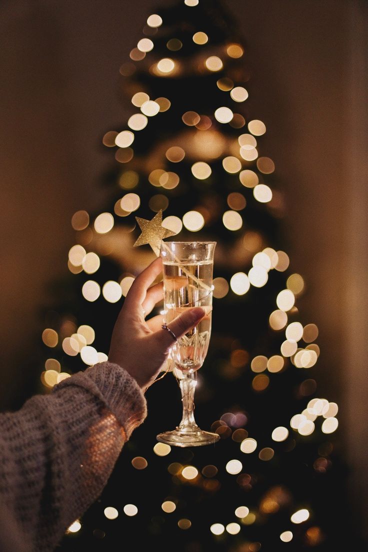 a person holding a wine glass in front of a christmas tree