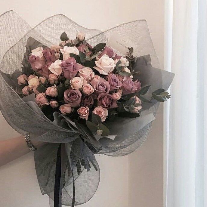 a person holding a bouquet of flowers in front of a white wall with a black ribbon