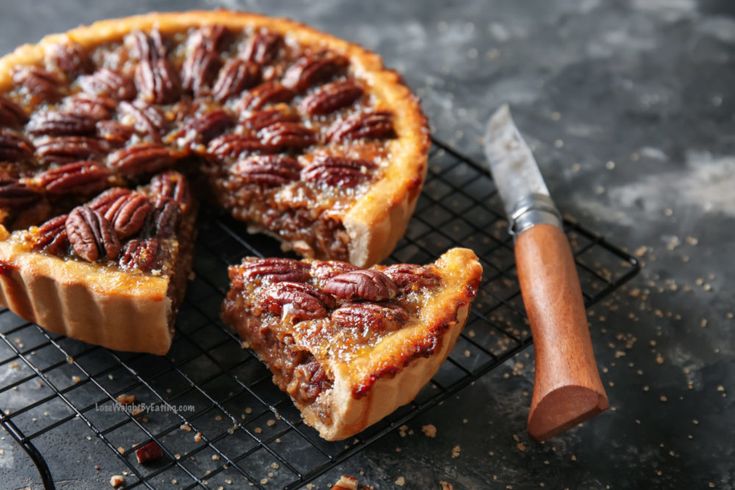 a pecan pie on a cooling rack next to a knife