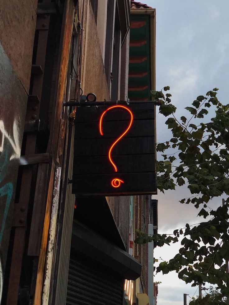 a neon question sign hanging from the side of a building