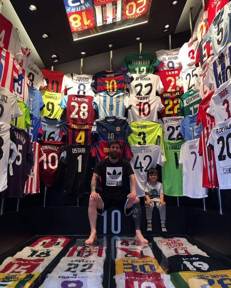 a man sitting on top of a table in front of many soccer jersey hanging from the ceiling