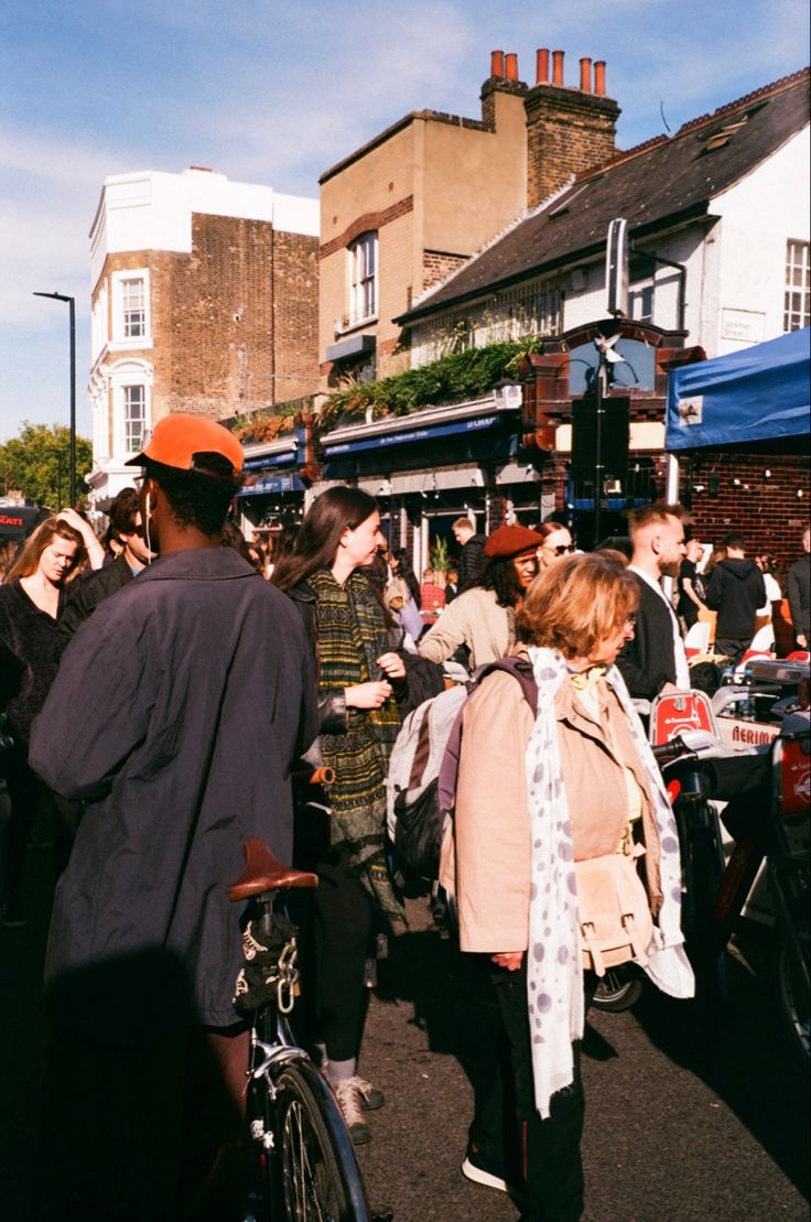 a group of people walking down a street next to tall buildings and parked bicycles in front of them