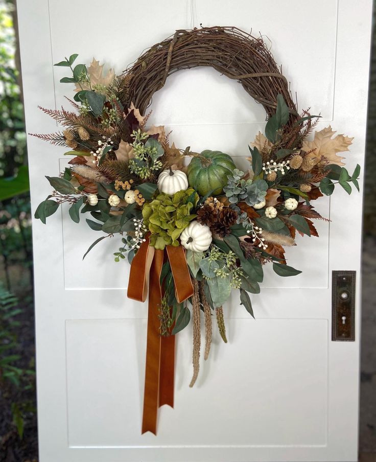 a wreath is hanging on the door with fall foliages and pumpkins in it