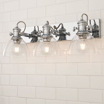 a bathroom light fixture with four lights on the side and white brick wall behind it