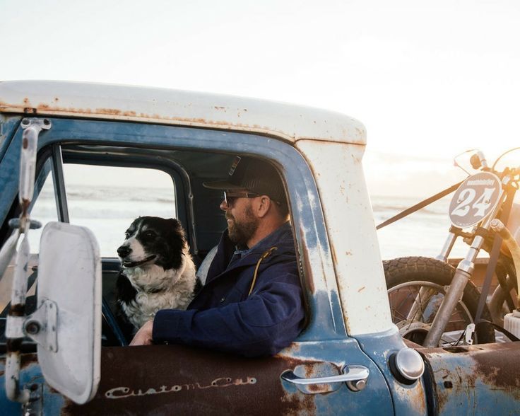 a man sitting in the drivers seat of an old truck with his dog