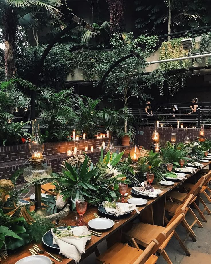 a long table is set with plates and place settings for an outdoor dinner in the jungle