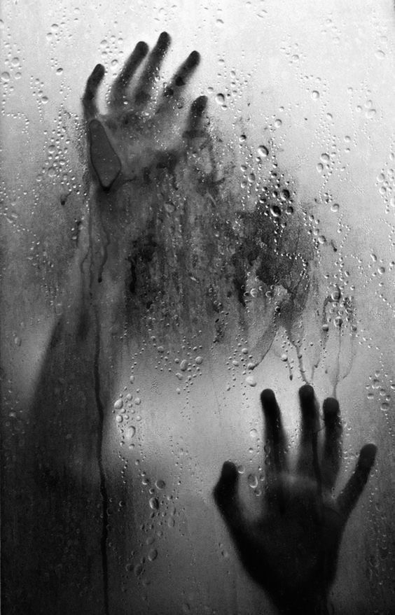 a person's hand is seen through a window with water droplets on it and the background is black and white