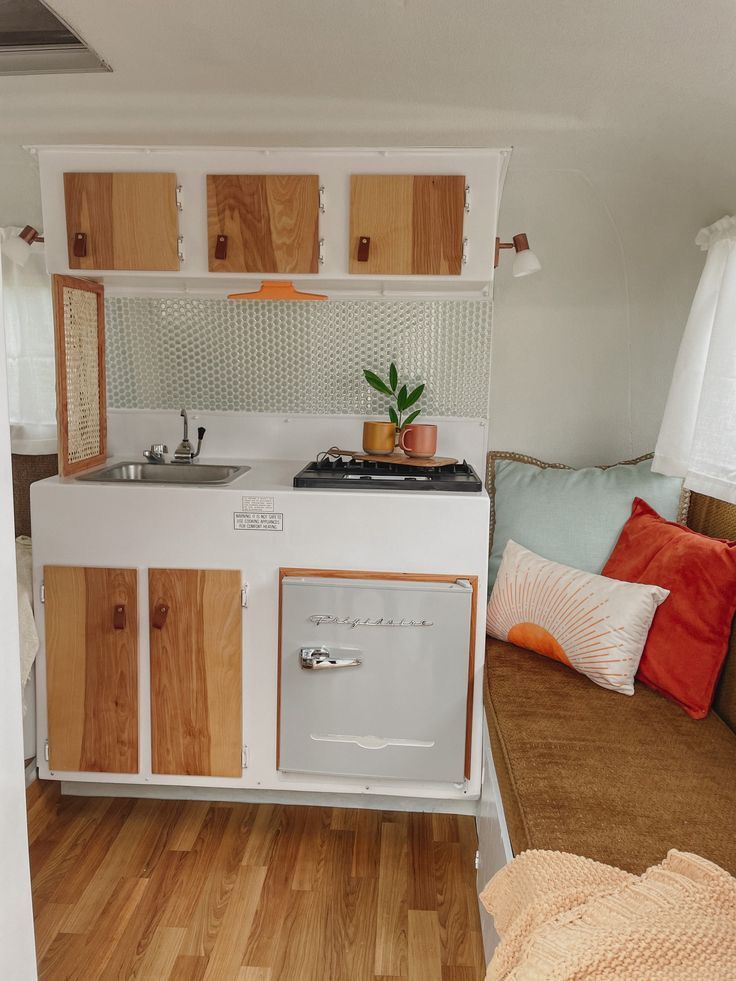 a small kitchen with wood flooring and white appliances on the wall, next to a couch