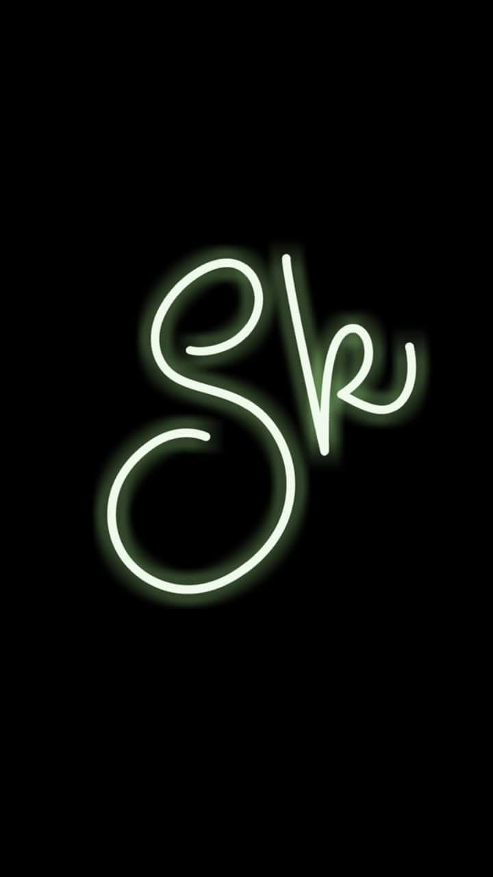 the letter s is made up of neon green lights on a black background, and it appears to be spelled in cursive letters