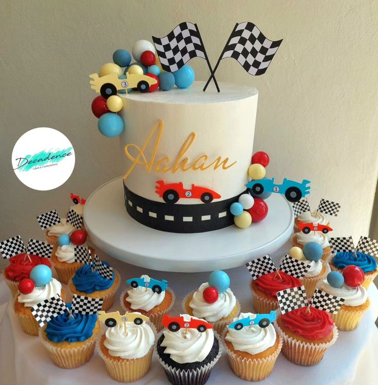 a birthday cake with cupcakes and race flags around it on a white table