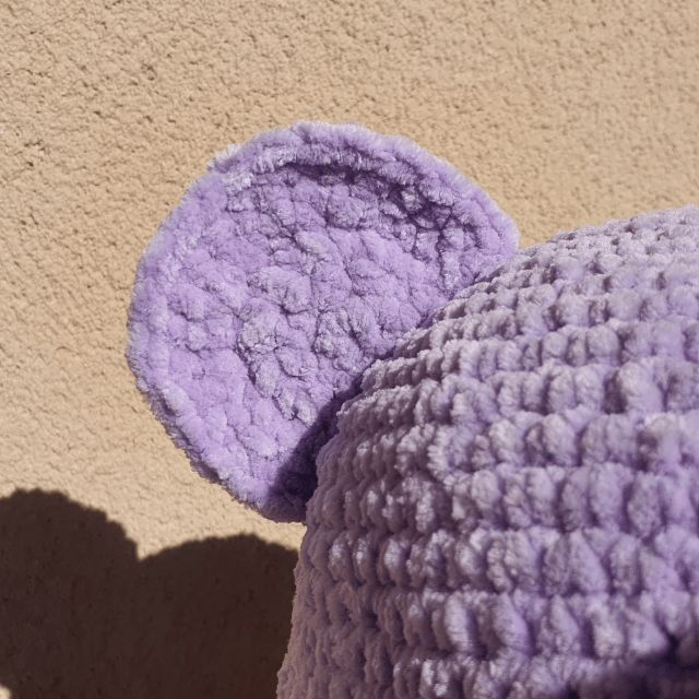 there is a purple hat with ears on the top and bottom, next to a tan wall