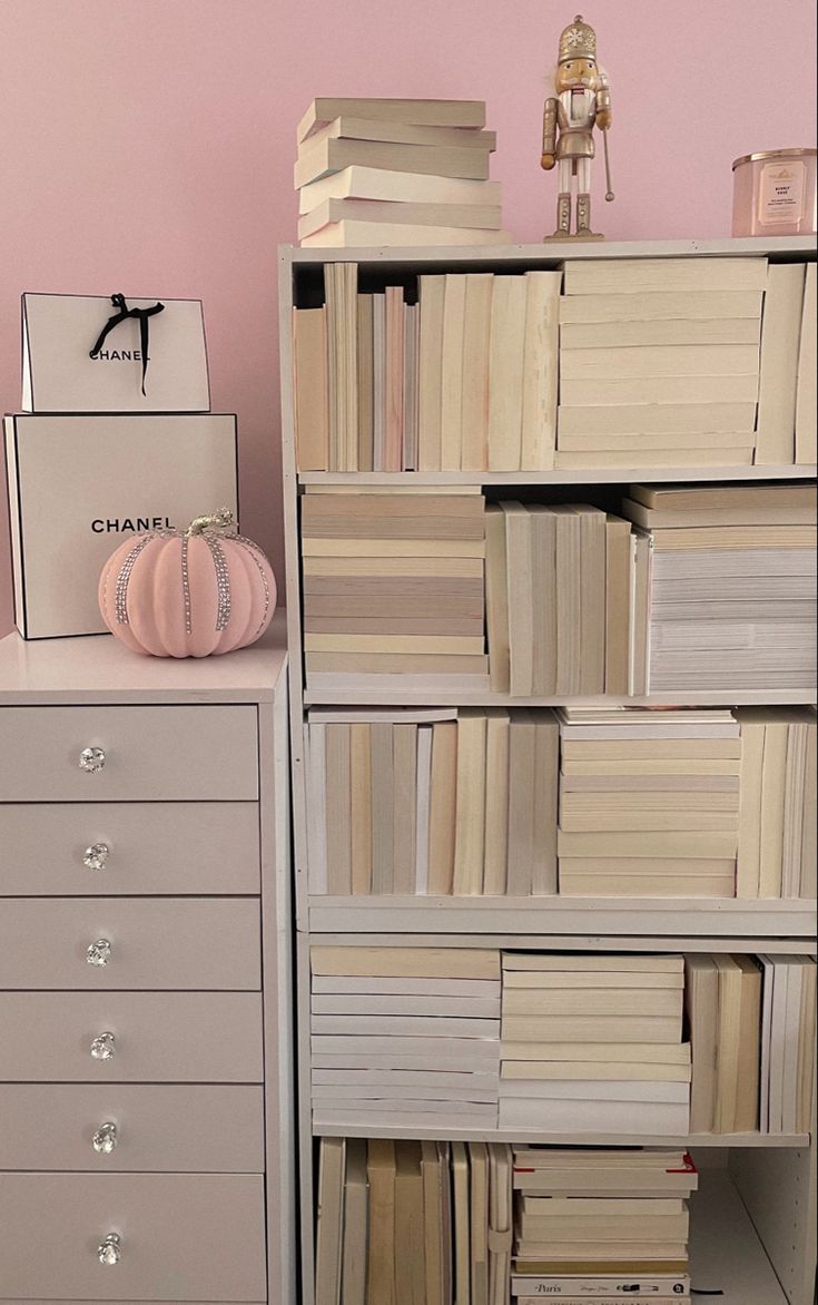 a book shelf filled with lots of books next to a white dresser and pink wall