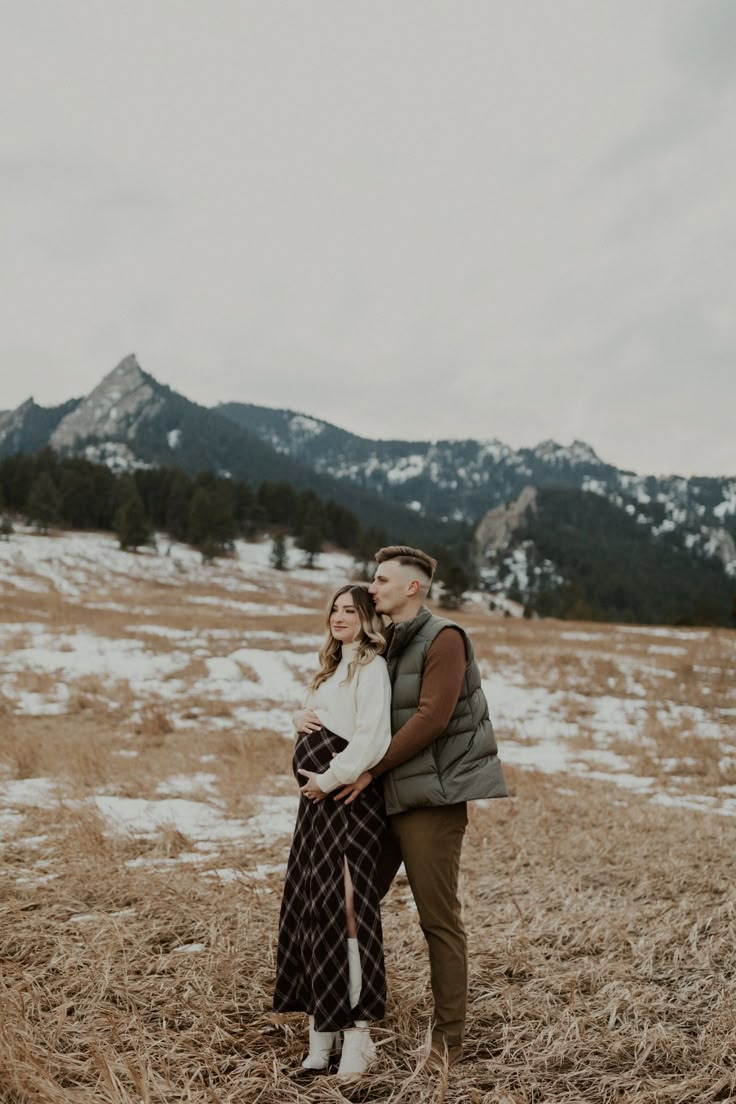 an engaged couple standing in a field with mountains in the background