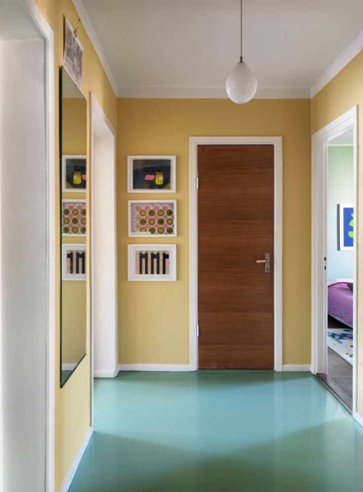 an empty hallway with yellow walls and green flooring is pictured in this image, there are pictures on the wall above the door