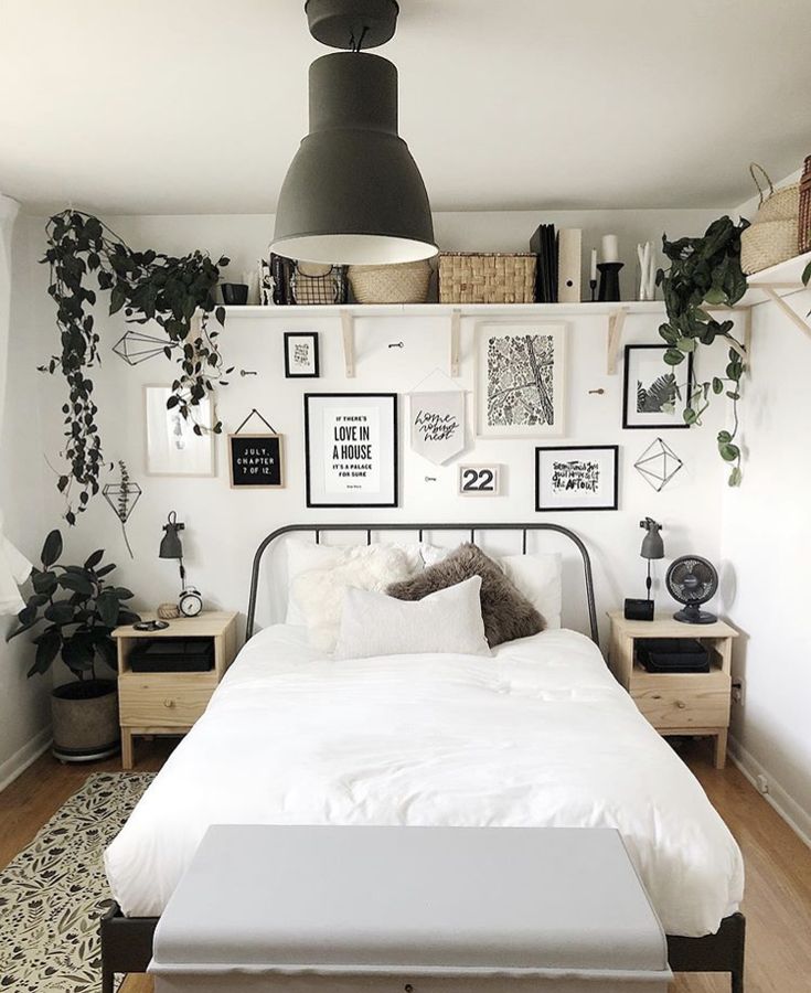 a white bed sitting in a bedroom next to a wall with pictures and plants on it