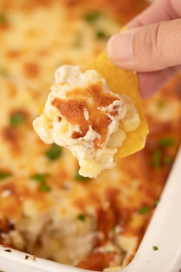 a hand holding a cracker over a casserole dish with chicken and cheese