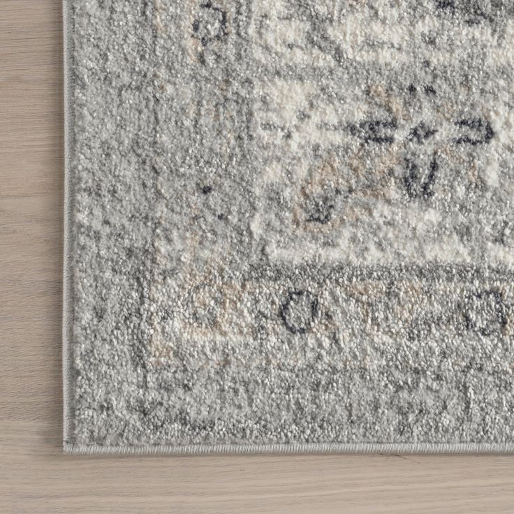 an area rug with a gray and white design on the top, in front of a wooden floor