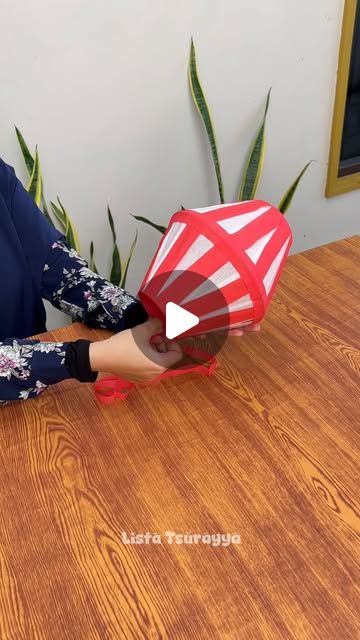 a woman sitting at a wooden table holding a red and white object in front of her face