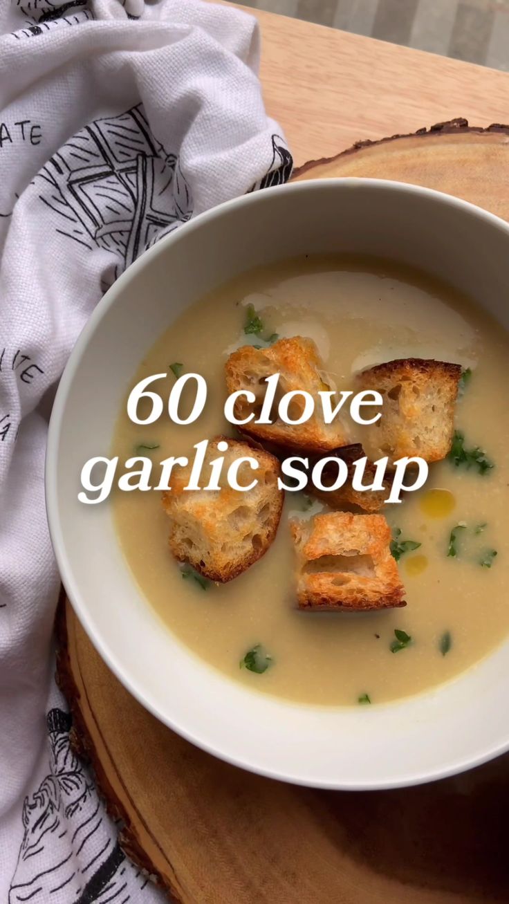 a white bowl filled with soup and croutons on top of a wooden table