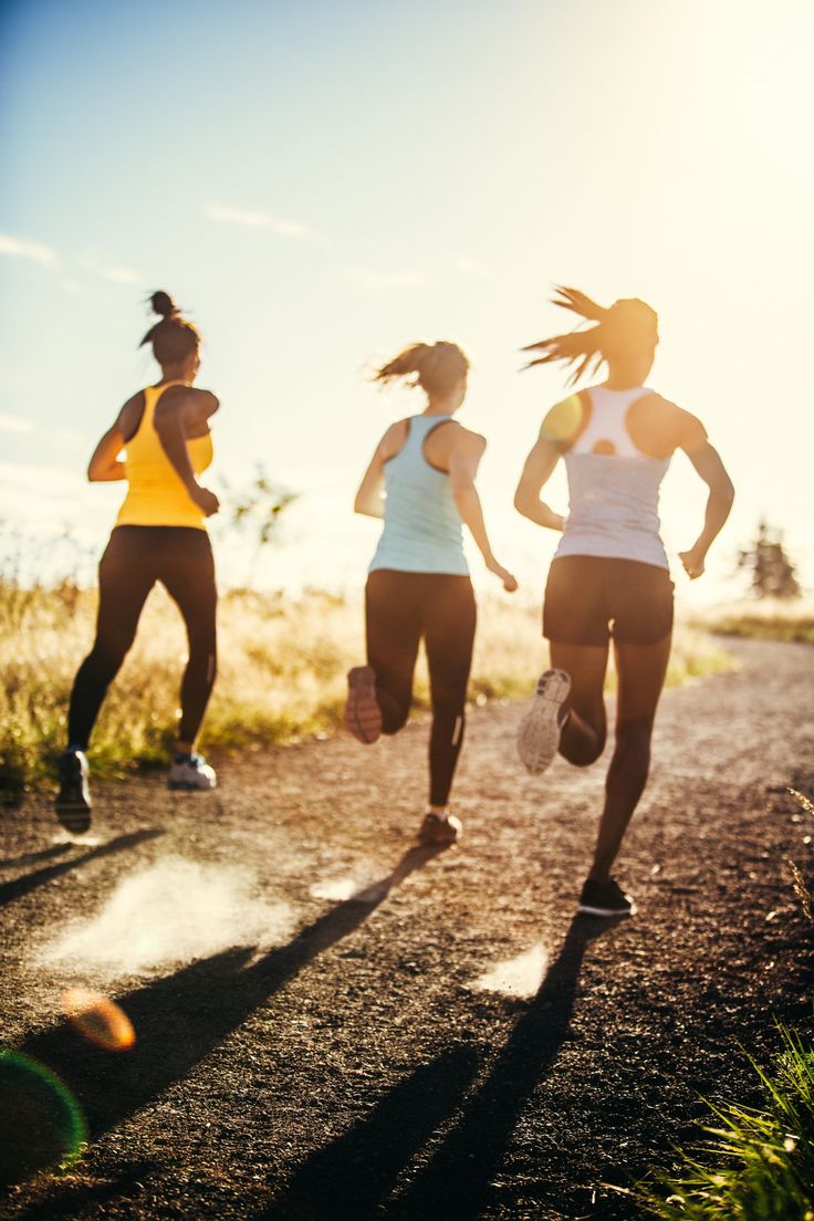 three women running down a dirt road with the sun shining on them and grass in the foreground