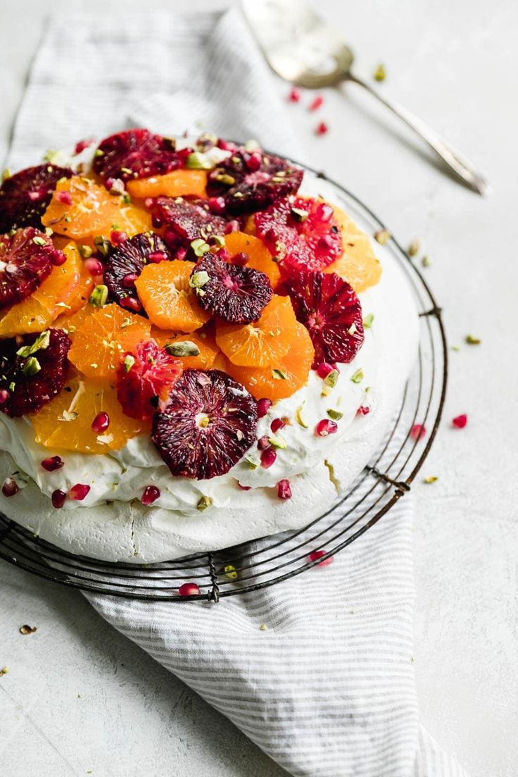 a cake with oranges, cranberries and pistachio on top sits on a wire rack