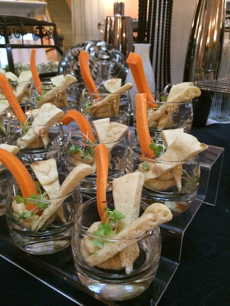 small glass dishes with carrots and crackers in them sitting on a black table