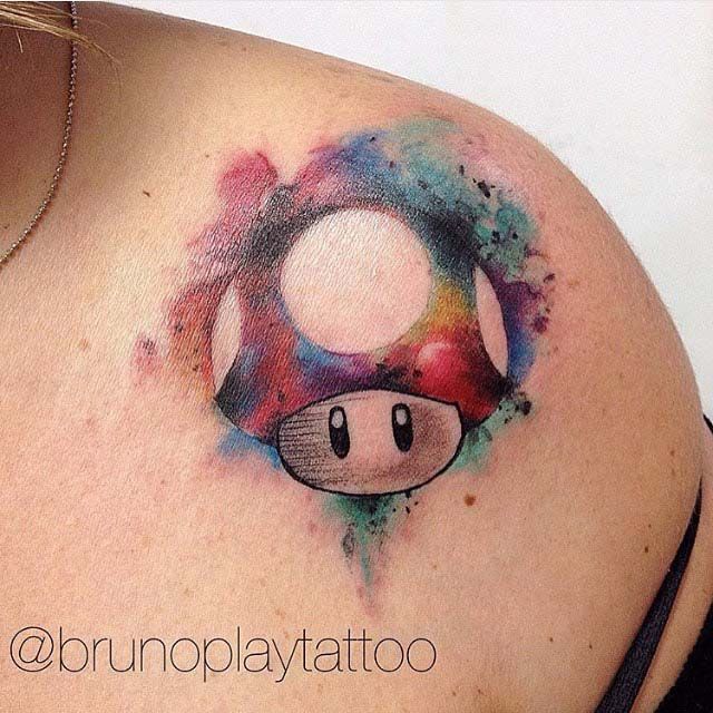 a woman's back shoulder with a mushroom tattoo on her left shoulder and watercolor paint splatters all over it