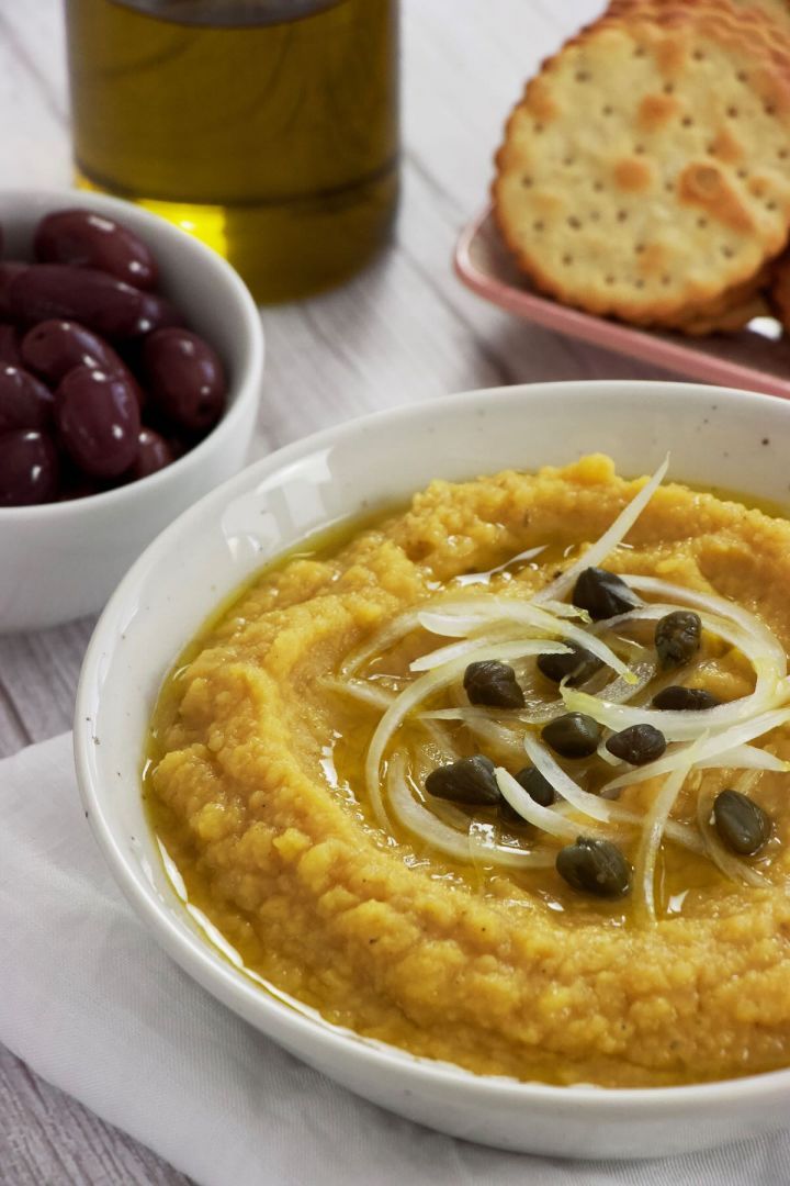 a bowl of hummus with olives and crackers