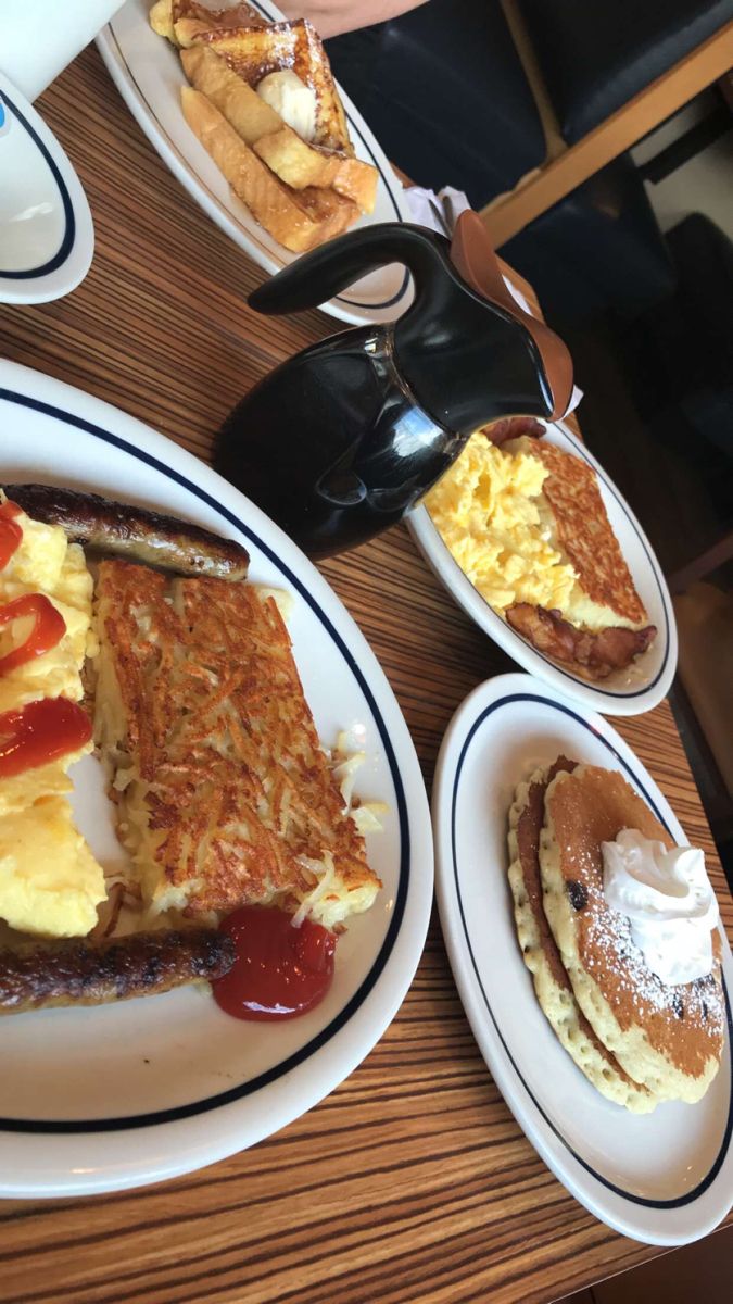 pancakes, eggs, and other breakfast foods are on plates at a table with coffee