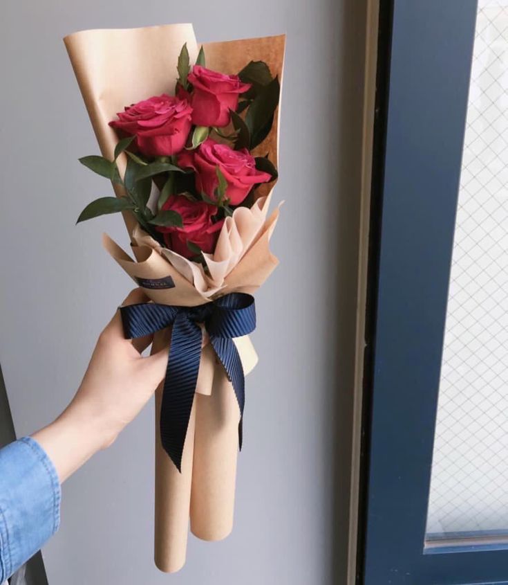 someone is holding a bouquet of roses in their hand and the flowers are wrapped in brown paper