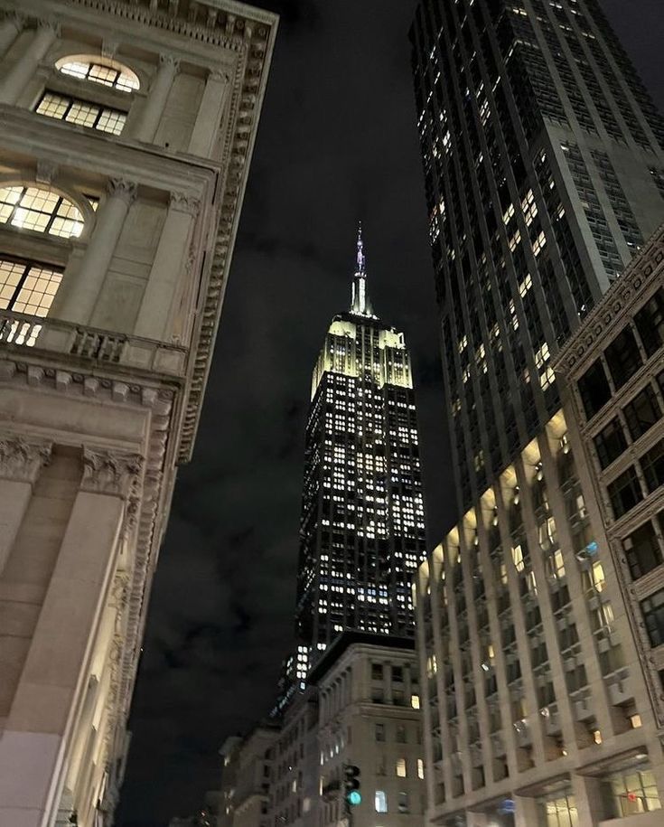 the empire building is lit up at night in new york city, ny on a cloudy day