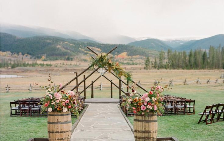 an outdoor ceremony set up with wooden barrels and floral centerpieces on the aisle