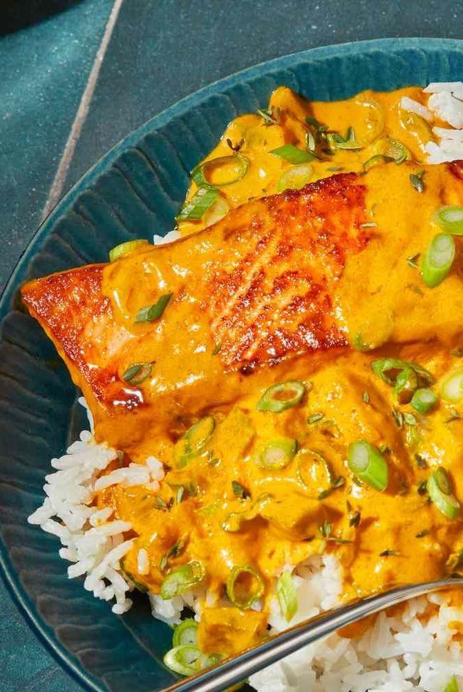 a blue plate topped with rice and meat covered in sauce next to a fork on top of it