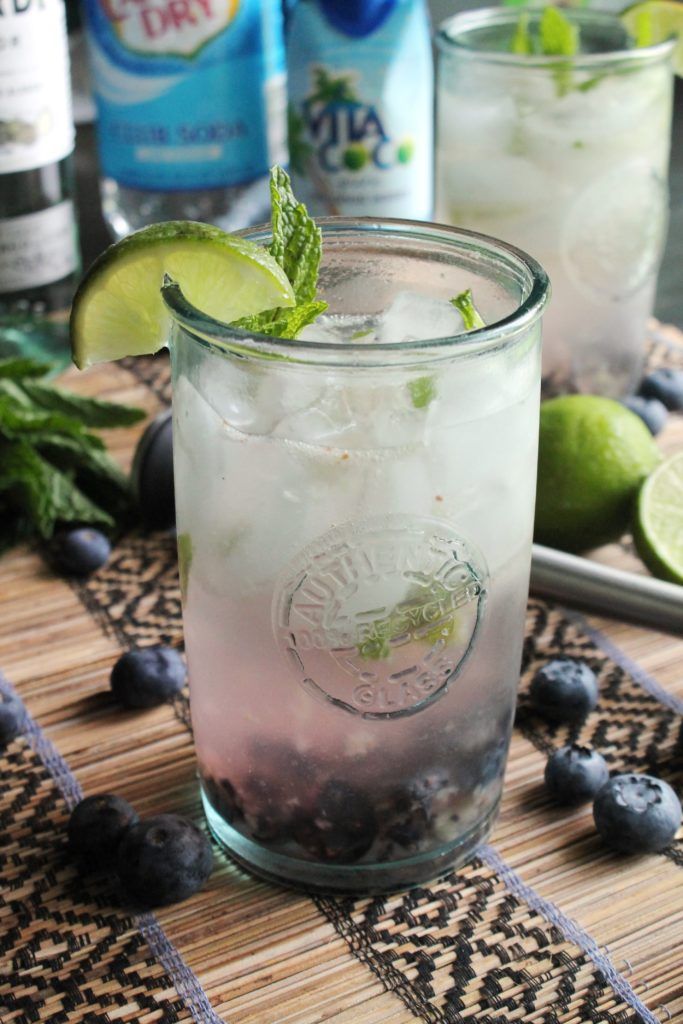 two glasses filled with blueberries and limeade on top of a table