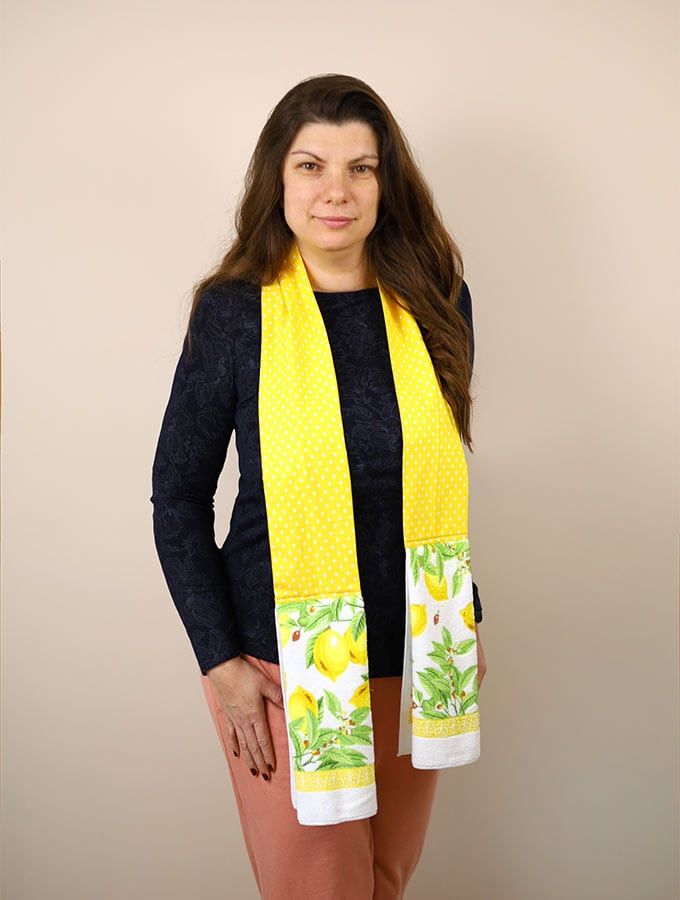 a woman standing in front of a wall wearing a yellow scarf