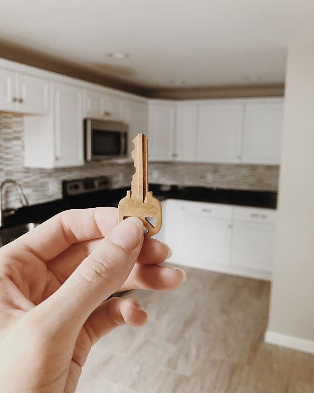 a person holding a key in front of an open kitchen with white cabinets and wood floors