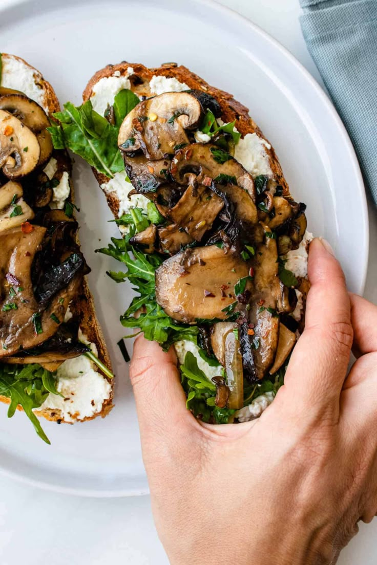 a person holding a sandwich with mushrooms on it