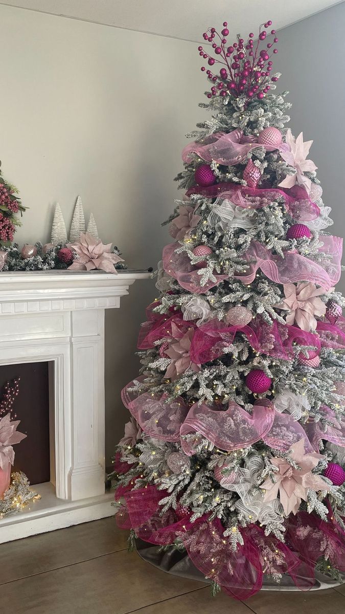 a pink and silver christmas tree in front of a fireplace with presents on the mantle