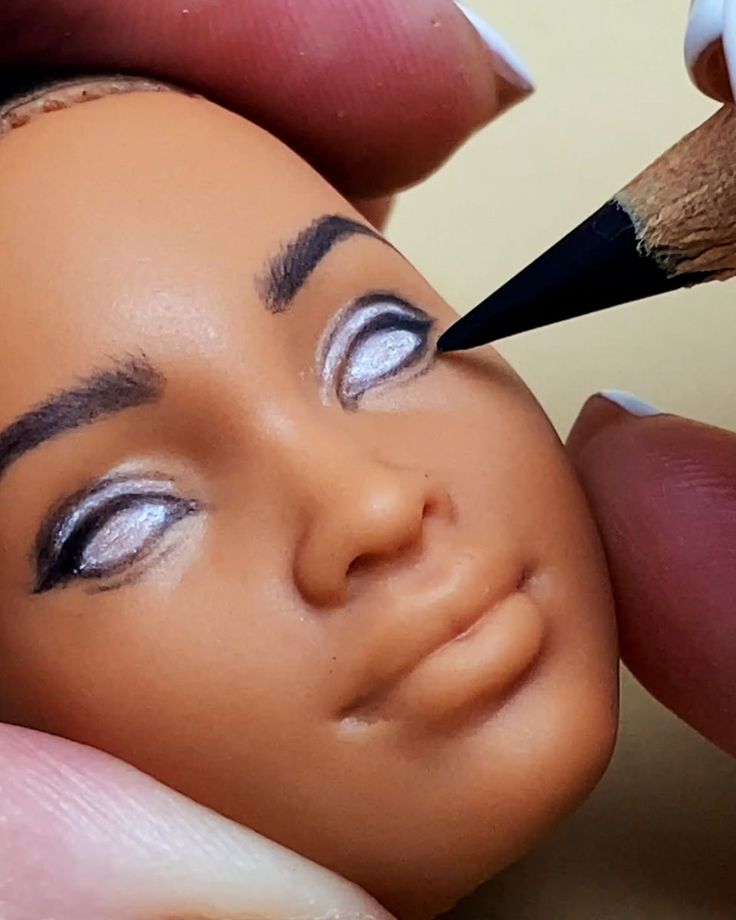 a close up of a person holding a pencil to a doll's face