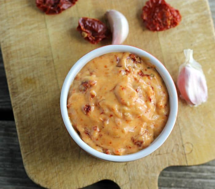 a white bowl filled with sauce sitting on top of a wooden cutting board next to garlic